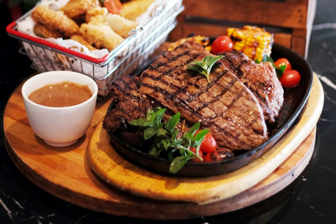 Grillplatte mit Steak, Pommes, Salat und Sauce auf einem Holzbrett